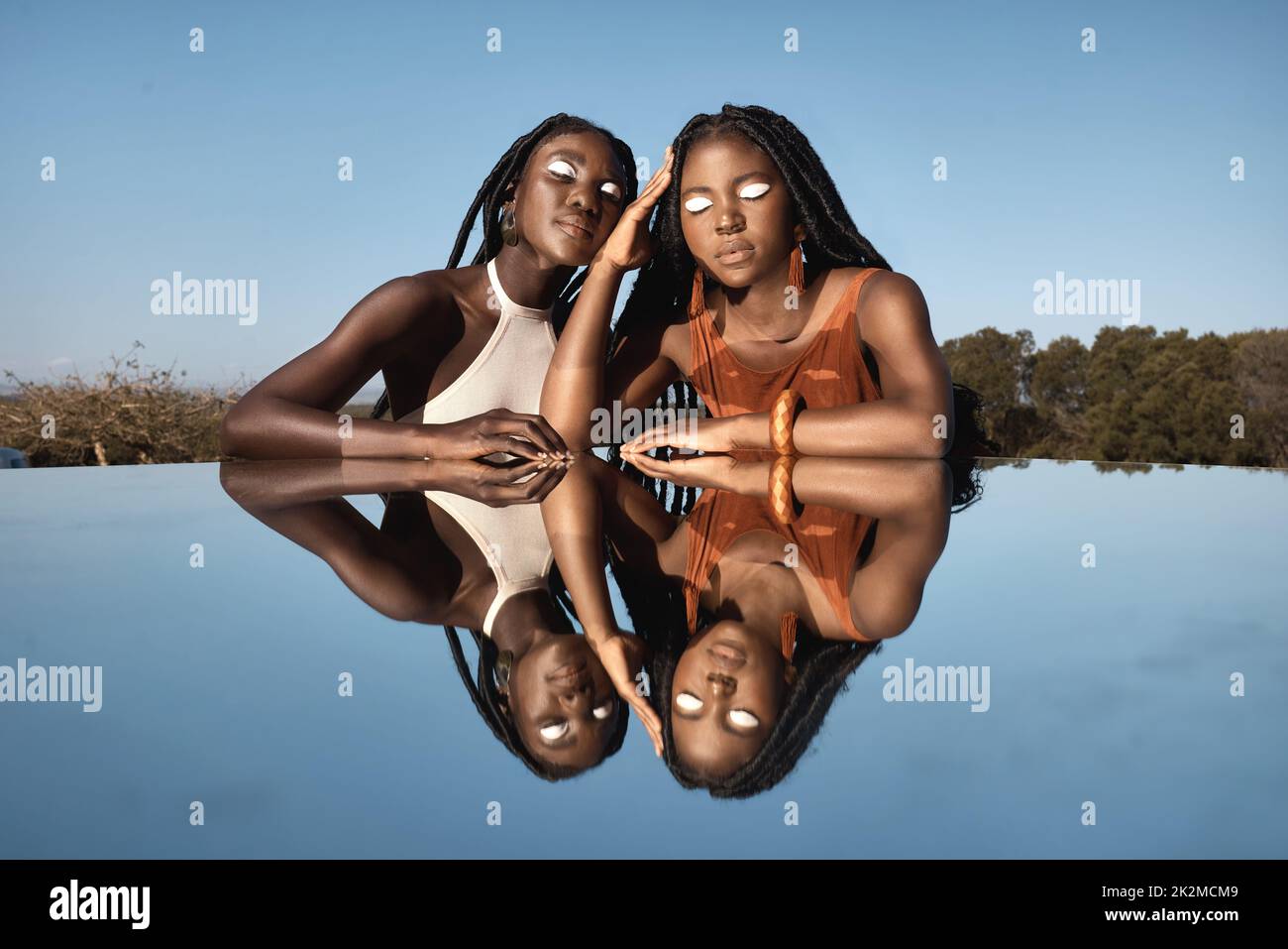 Indivis et toujours unis. Photo de deux jeunes femmes attrayantes assises à côté d'un étang avec leur réflexion dans la nature. Banque D'Images