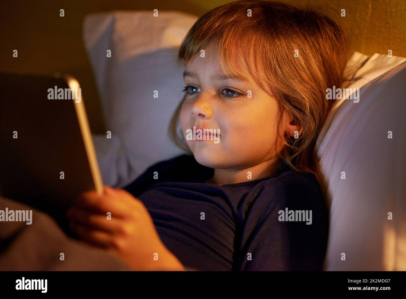 Lire mon histoire de coucher en ligne. Une petite fille au lit avec une tablette numérique. Banque D'Images