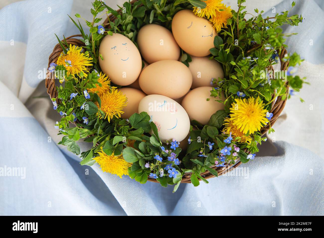 Beau bouquet de printemps dans un panier en bois avec des oeufs peints de Pâques, des oeufs avec des visages mignons. Banque D'Images