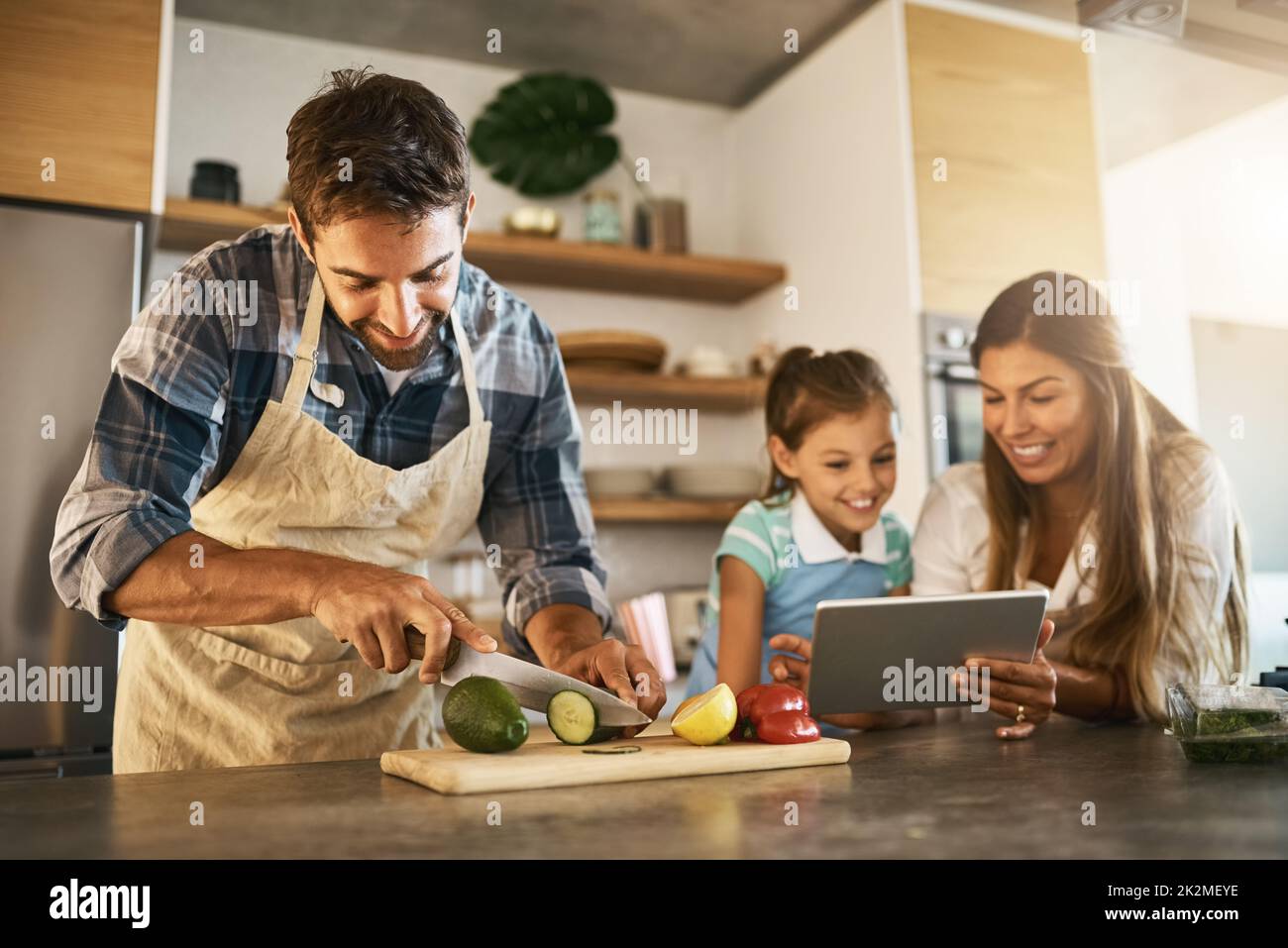 Cuisson selon leurs instructions. Photo de deux parents heureux et de leur jeune fille essayant ensemble une nouvelle recette dans la cuisine. Banque D'Images