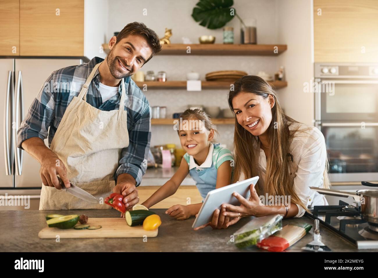 C'est ainsi que nous passons nos samedis. Portrait de deux parents heureux et de leur jeune fille essayant ensemble une nouvelle recette dans la cuisine. Banque D'Images