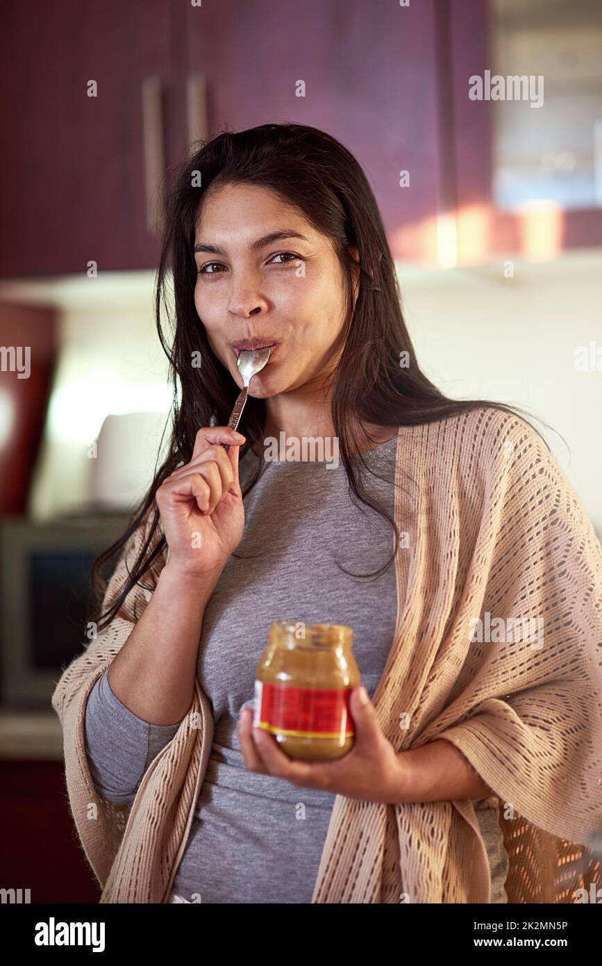 Se livrer à son plaisir coupable. Portrait d'une jeune femme heureuse mangeant du beurre d'arachide dans un pot tout en se tenant dans sa cuisine à la maison. Banque D'Images