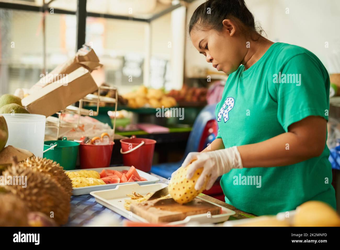 Seul le meilleur produit fait la coupe. Prise de vue d'une femme qui coupe des fruits dans un marché alimentaire thaïlandais. Banque D'Images