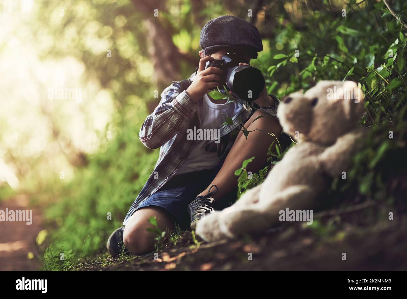 HES le petit photographe le plus mignon. Prise de vue d'un jeune garçon non identifiable à l'aide d'un appareil photo pour prendre des photos de sa peluche dans les bois. Banque D'Images