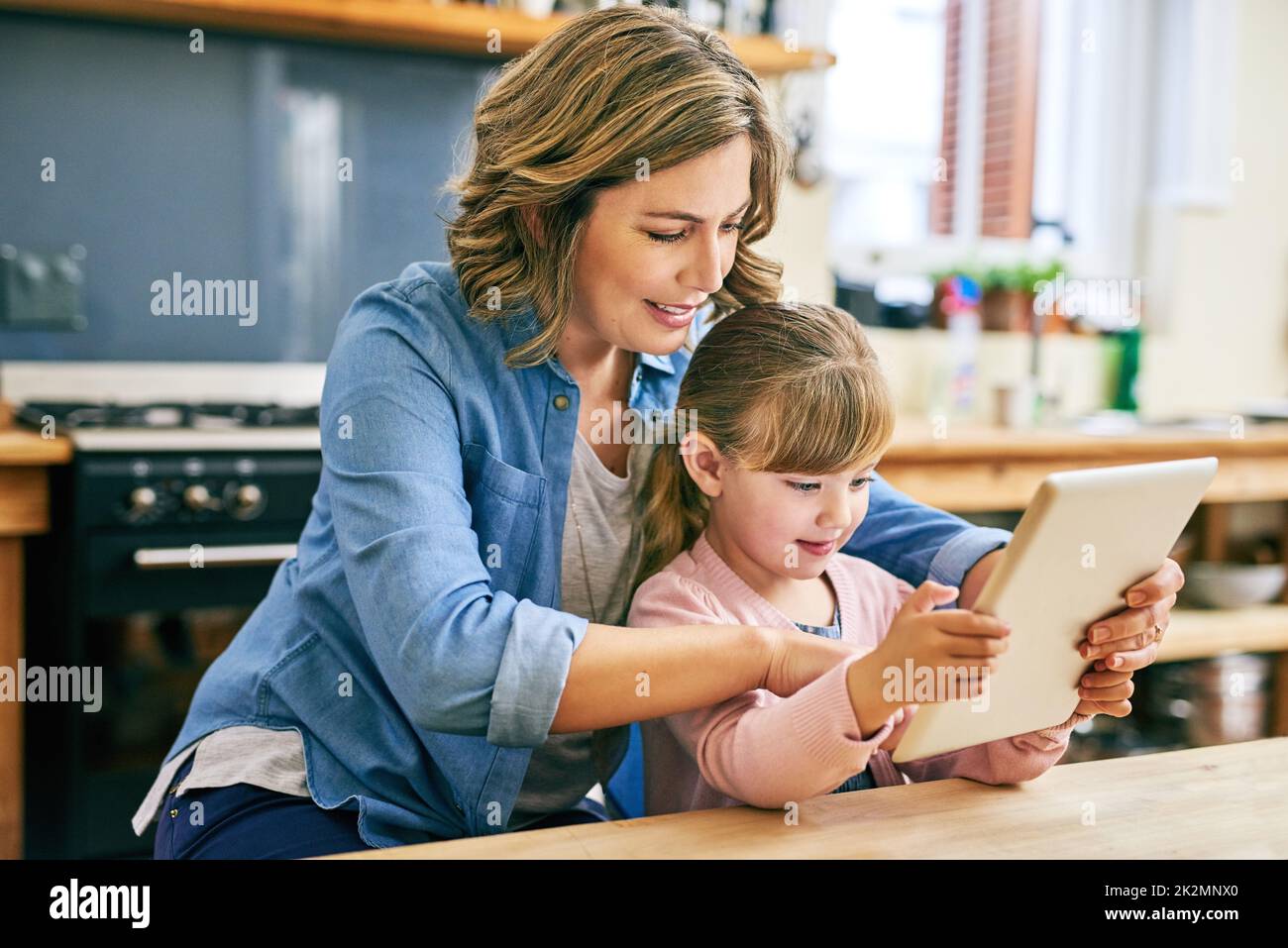 Nous pouvons comprendre cela ensemble. Photo d'une jeune mère gaie et de sa petite fille jouant autour d'une tablette numérique à la maison. Banque D'Images