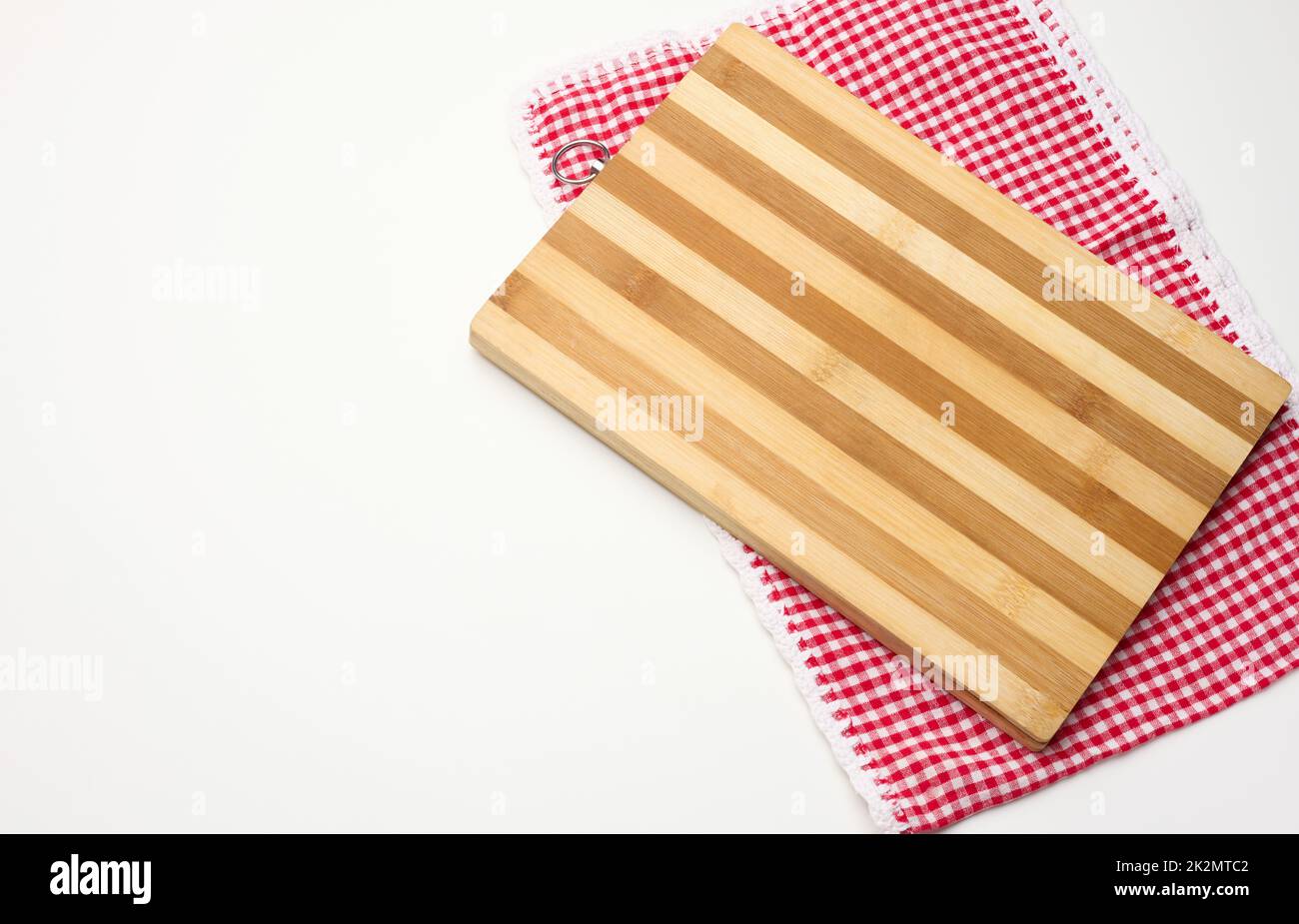 une planche à découper rectangulaire en bois vide et une serviette rouge dans une cage blanche sur une table blanche, vue du dessus Banque D'Images