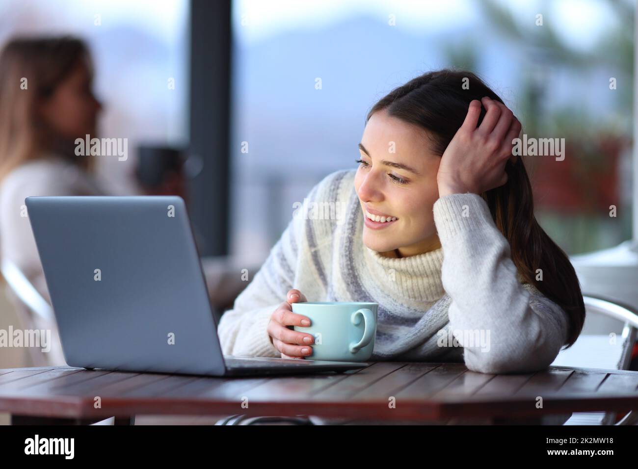 Bonne femme en hiver regardant les médias sur un ordinateur portable dans un bar Banque D'Images