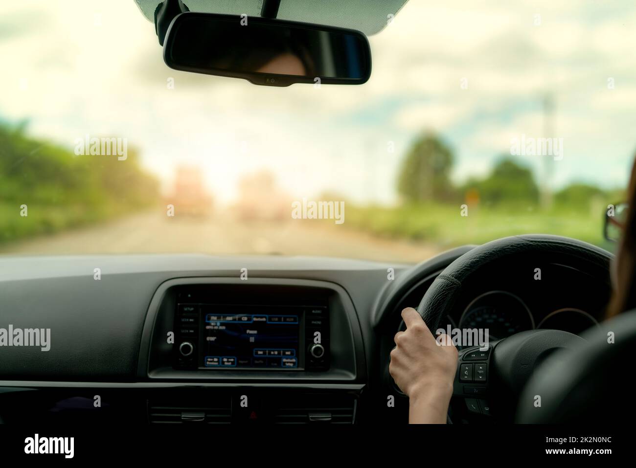 Vue arrière d'une femme en voiture pour un voyage d'été. Conduite en voiture avec sécurité sur route asphaltée. Main du conducteur tenant le volant pour contrôler le véhicule. Vue intérieure de la voiture. Tableau de bord et pare-brise. Banque D'Images