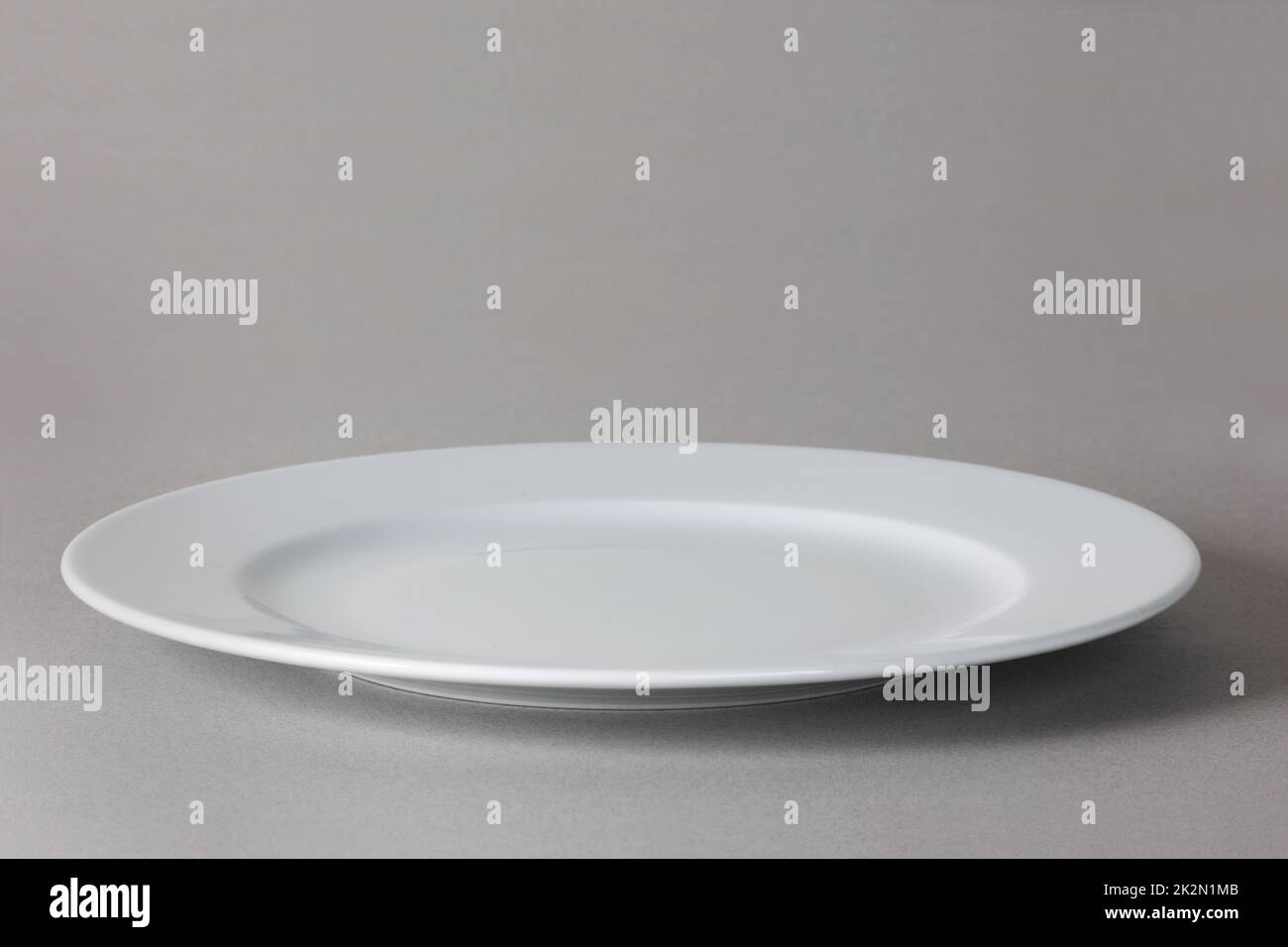 Vue angulaire d'une assiette à dîner blanche sur fond neutre avec ombre Banque D'Images