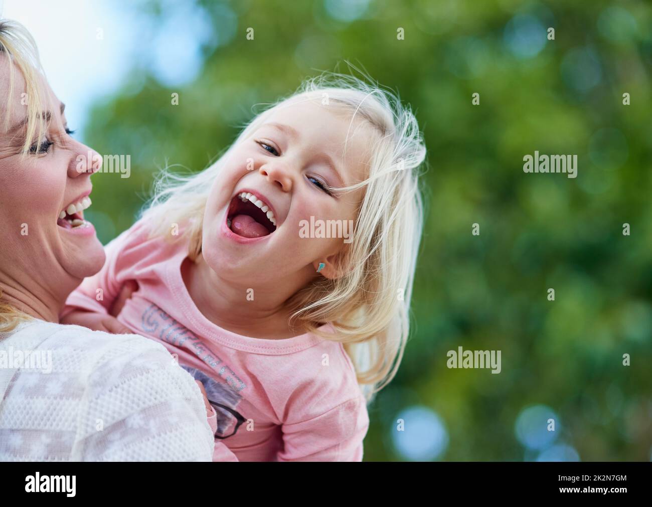 Theres rien de plus doux qu'un rire des enfants. Photo d'une petite fille mignonne qui rit tout en étant tenue par sa mère à l'extérieur. Banque D'Images