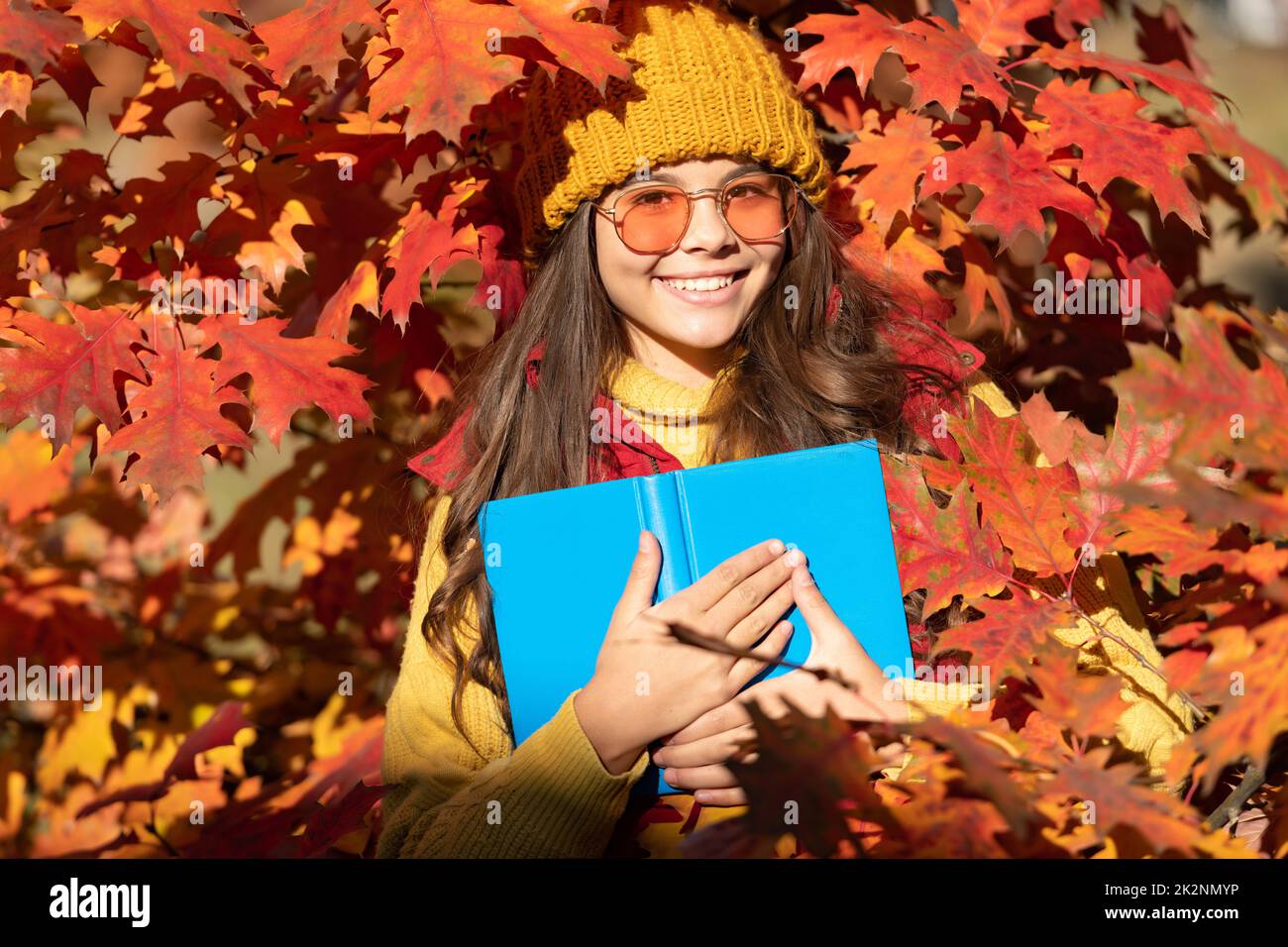 Visage de fille d'automne sur fond de feuille d'automne. Automne enfant adolescent fille 12, 13, 14 ans portrait. Heureux enfant tenir livre sur les feuilles d'automne Banque D'Images