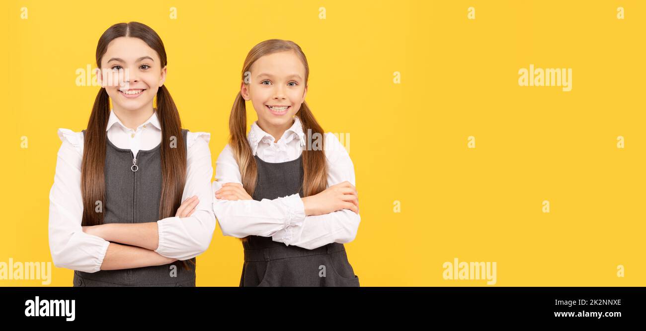 Filles d'école amis. Les enfants heureux portent l'uniforme d'école en gardant les bras croisés fond jaune, 1 septembre. Affiche horizontale isolée de fille d'école Banque D'Images
