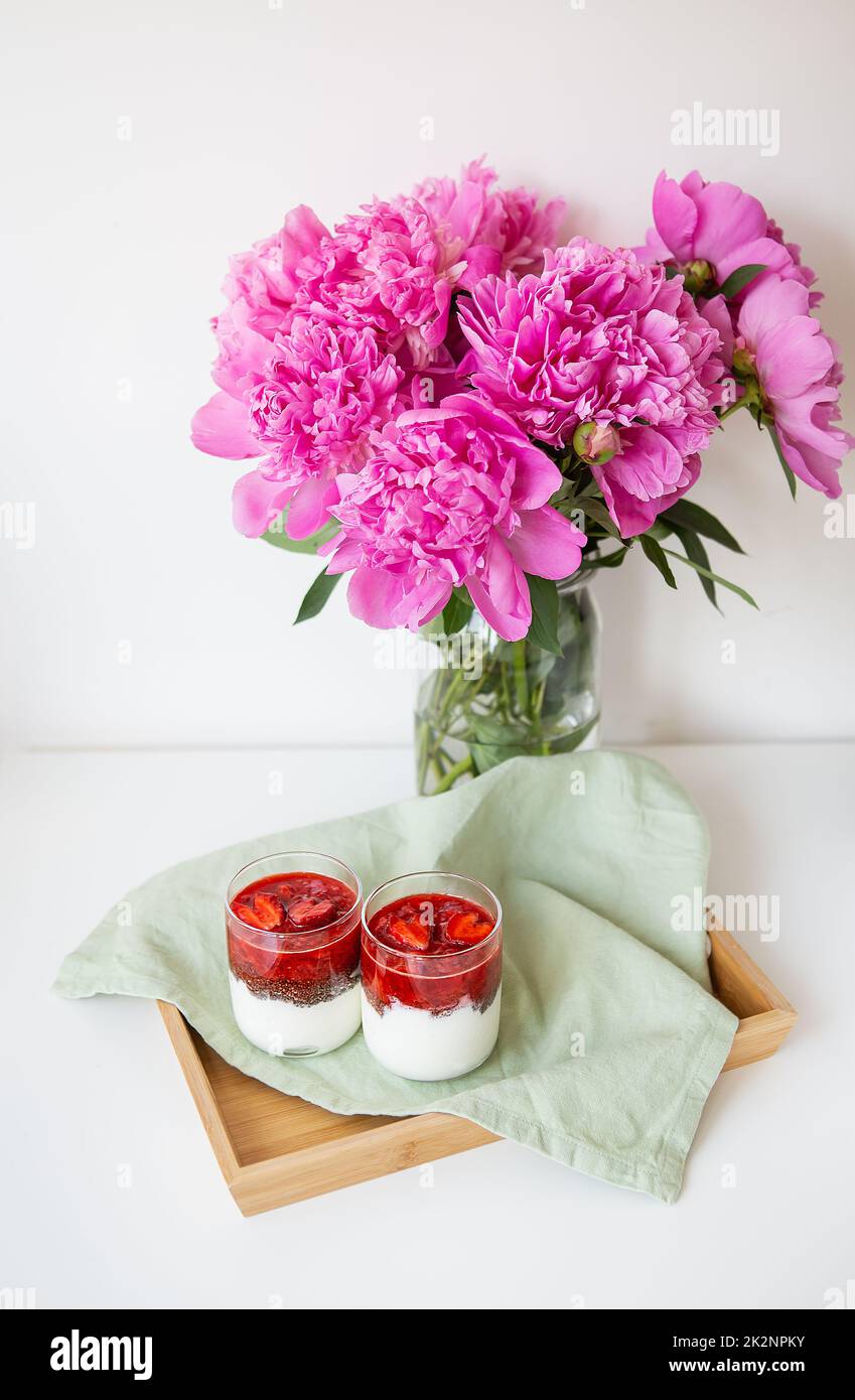 Un beau bouquet de pivoines roses dans un vase sur une table blanche est accompagné d'un dessert de fraise en forme de coeur. Saint-Valentin, 8 mars. Banque D'Images