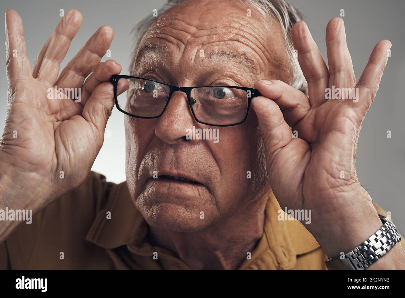 Je n'arrive pas à croire ce que je viens de voir. Prise de vue en studio d'un homme âgé qui ajuste ses lunettes sur fond gris. Banque D'Images