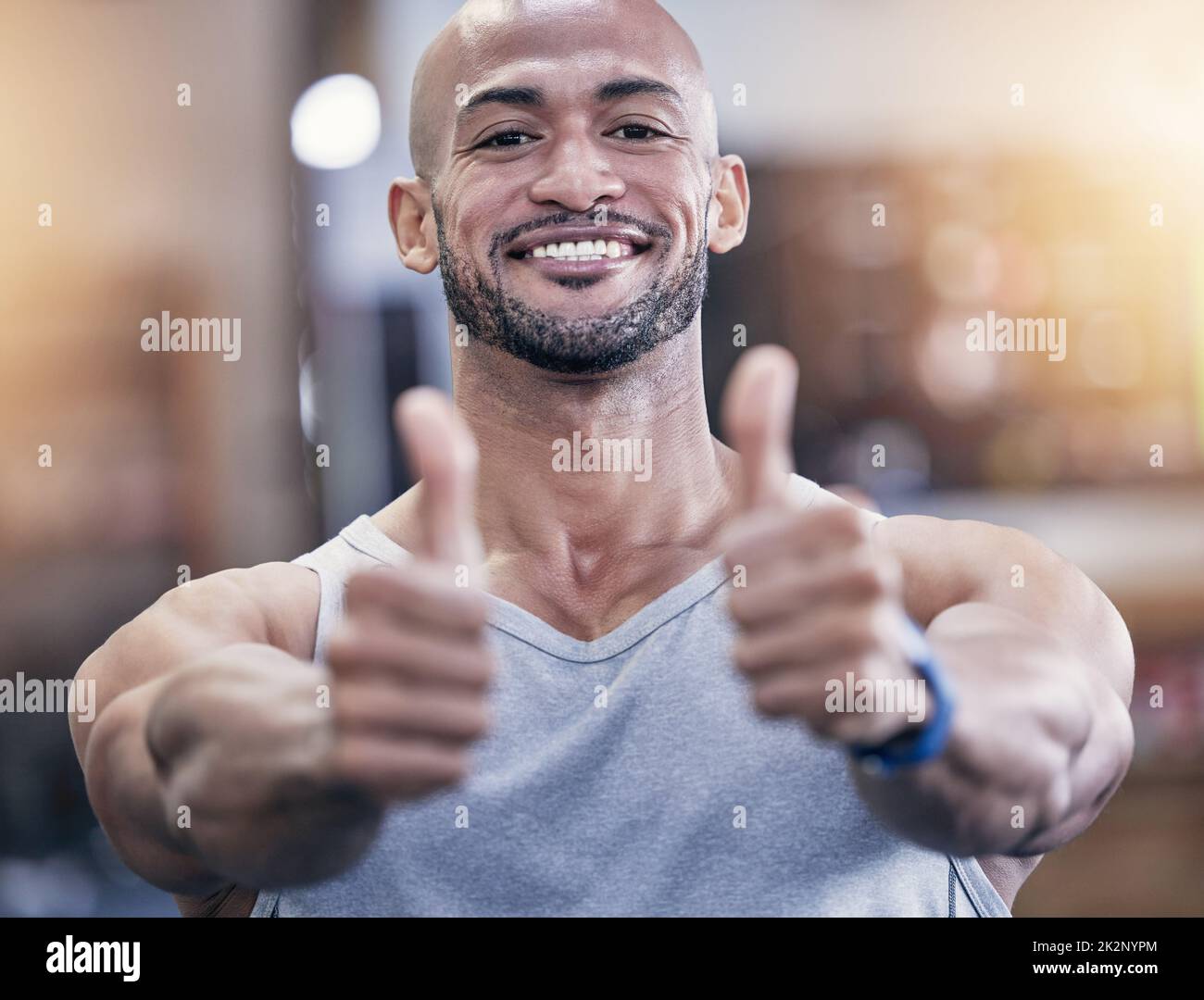 Ici pour accompagner votre voyage de remise en forme qui change la vie. Portrait d'un jeune homme musclé montrant les pouces vers le haut dans une salle de sport. Banque D'Images