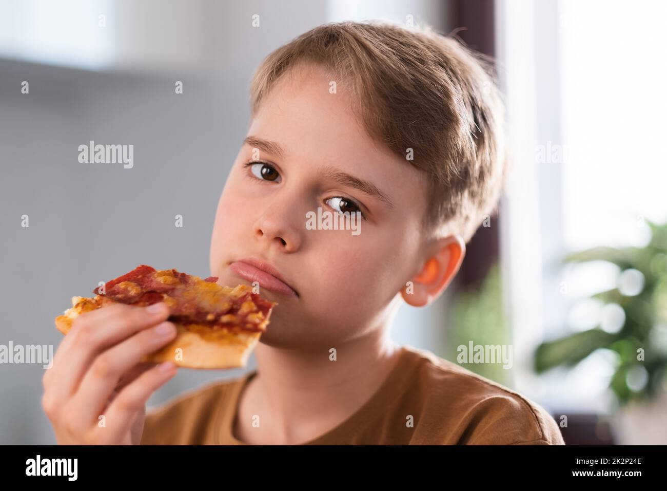 Un jeune garçon triste qui apprécie de manger une délicieuse pizza à la maison. Banque D'Images