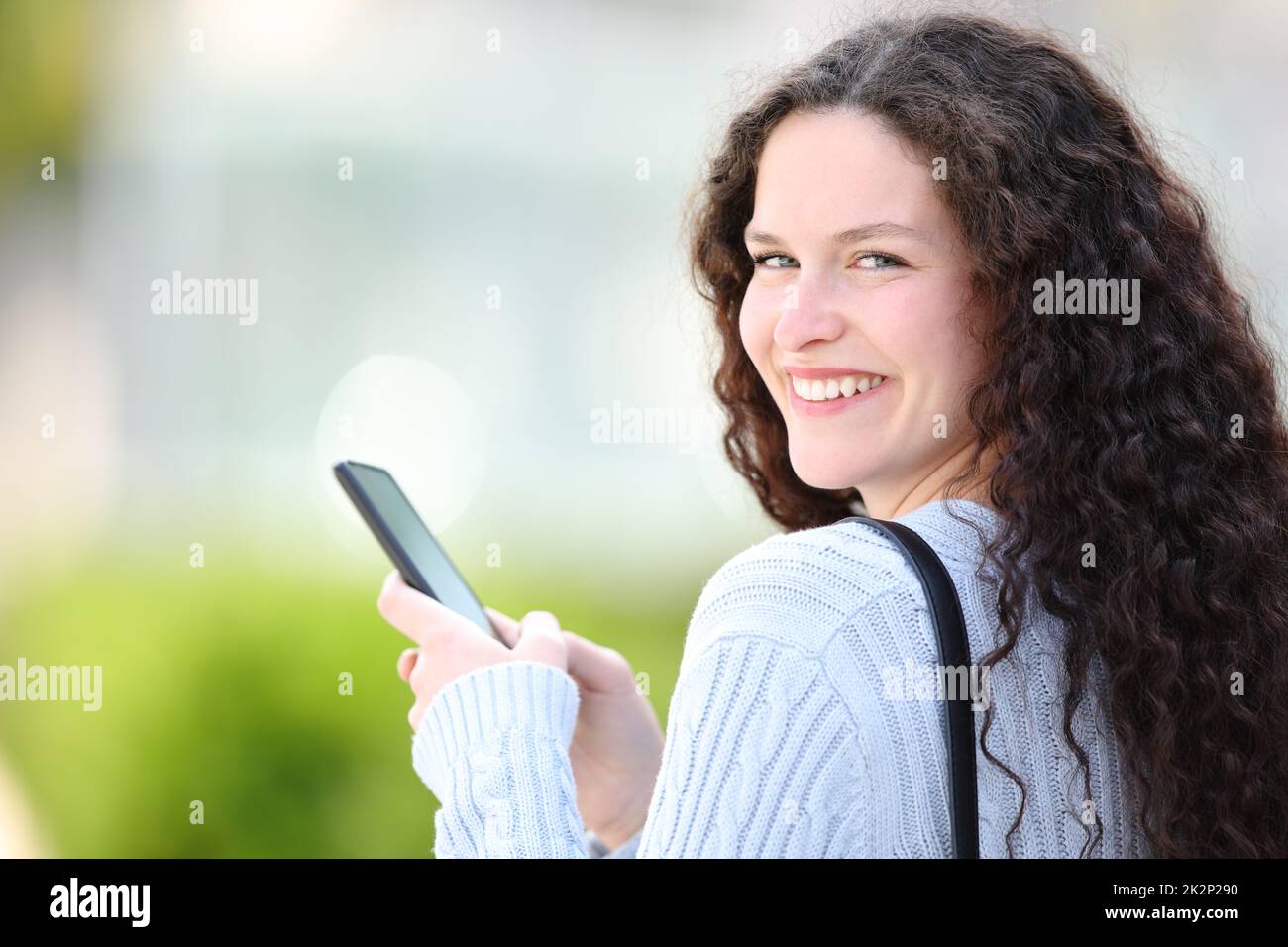 Une femme heureuse tenant un téléphone portable regarde l'appareil photo dans la rue Banque D'Images