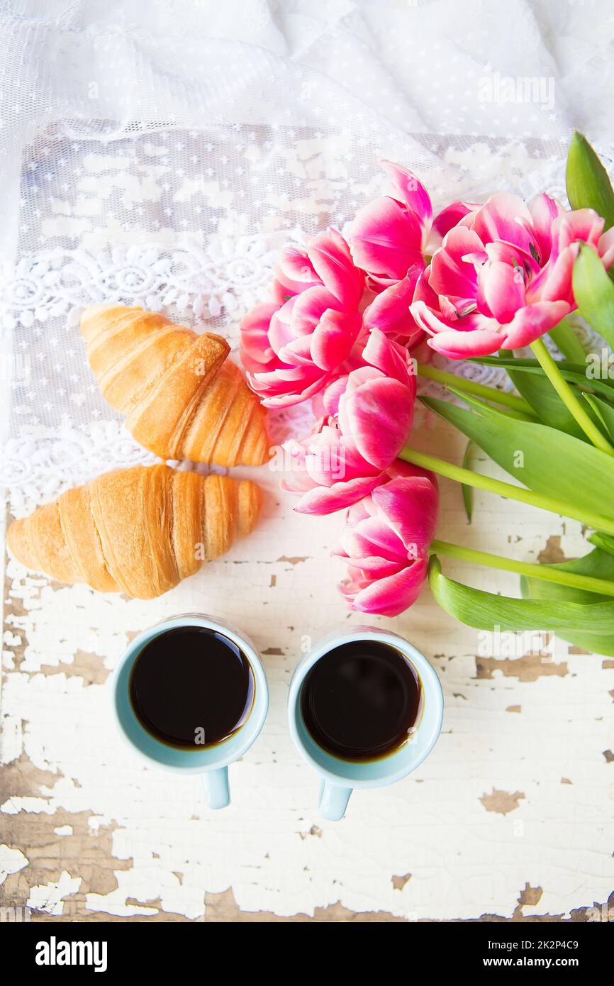 une bonne tasse de café, des croissants et des tulipes roses sur une vieille table blanche, en gros plan Banque D'Images