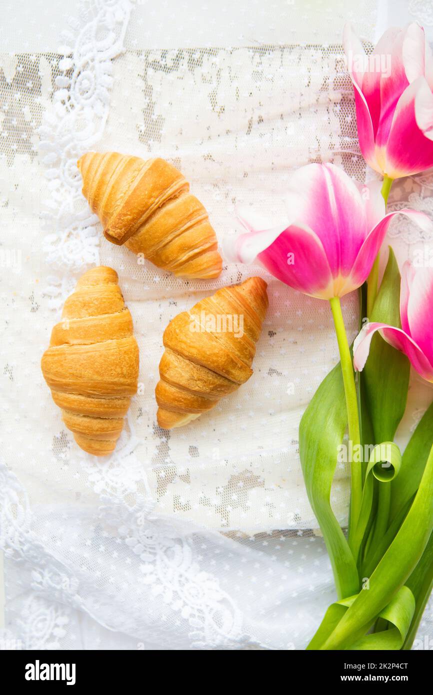 Trois croissants et de tulipes rose vif sur nappe en dentelle, close-up Banque D'Images