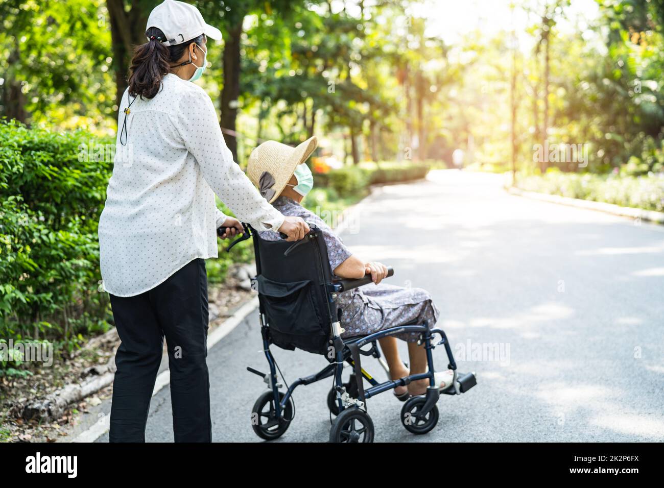 Aide-soignant et soins asiatique senior ou âgée vieille femme patiente assise en fauteuil roulant et portant un masque facial pour voyager dans le parc Banque D'Images