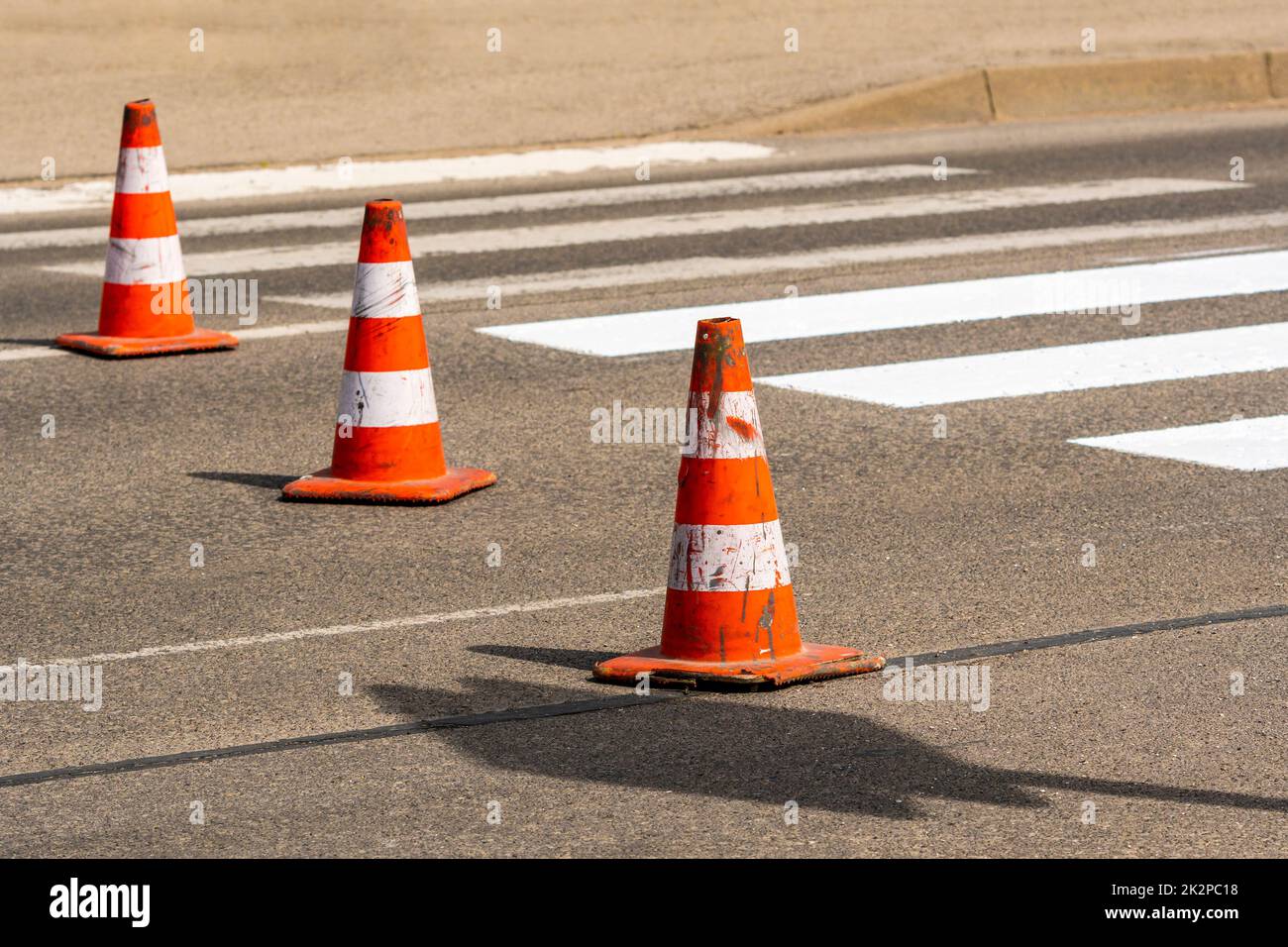 Cônes de signalisation avec bandes orange et blanches sur la rue sur asphalte gris pendant les travaux de construction de routes Banque D'Images
