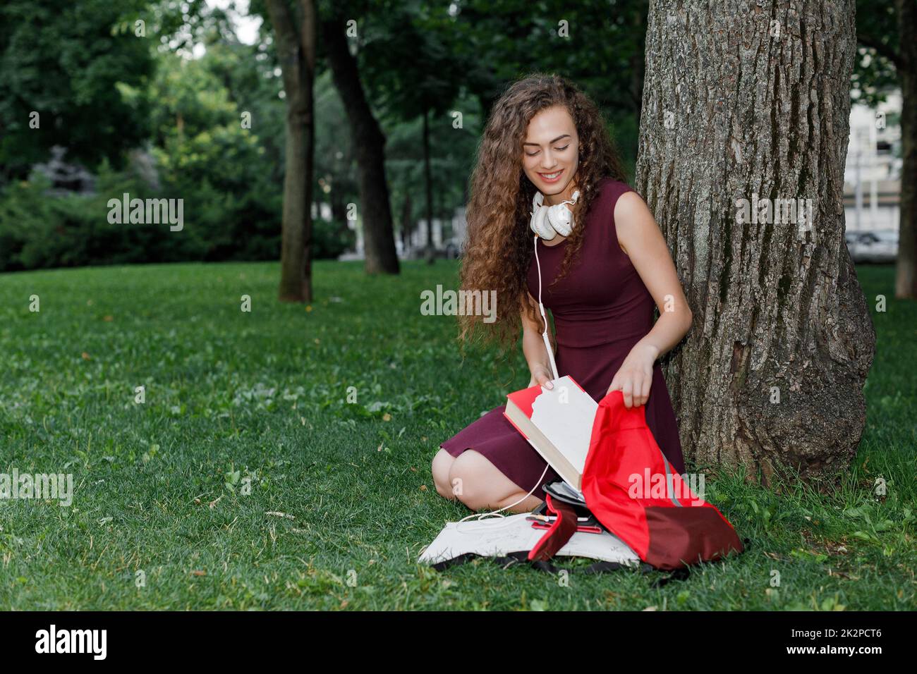 Girl student holding book et assis under tree Banque D'Images