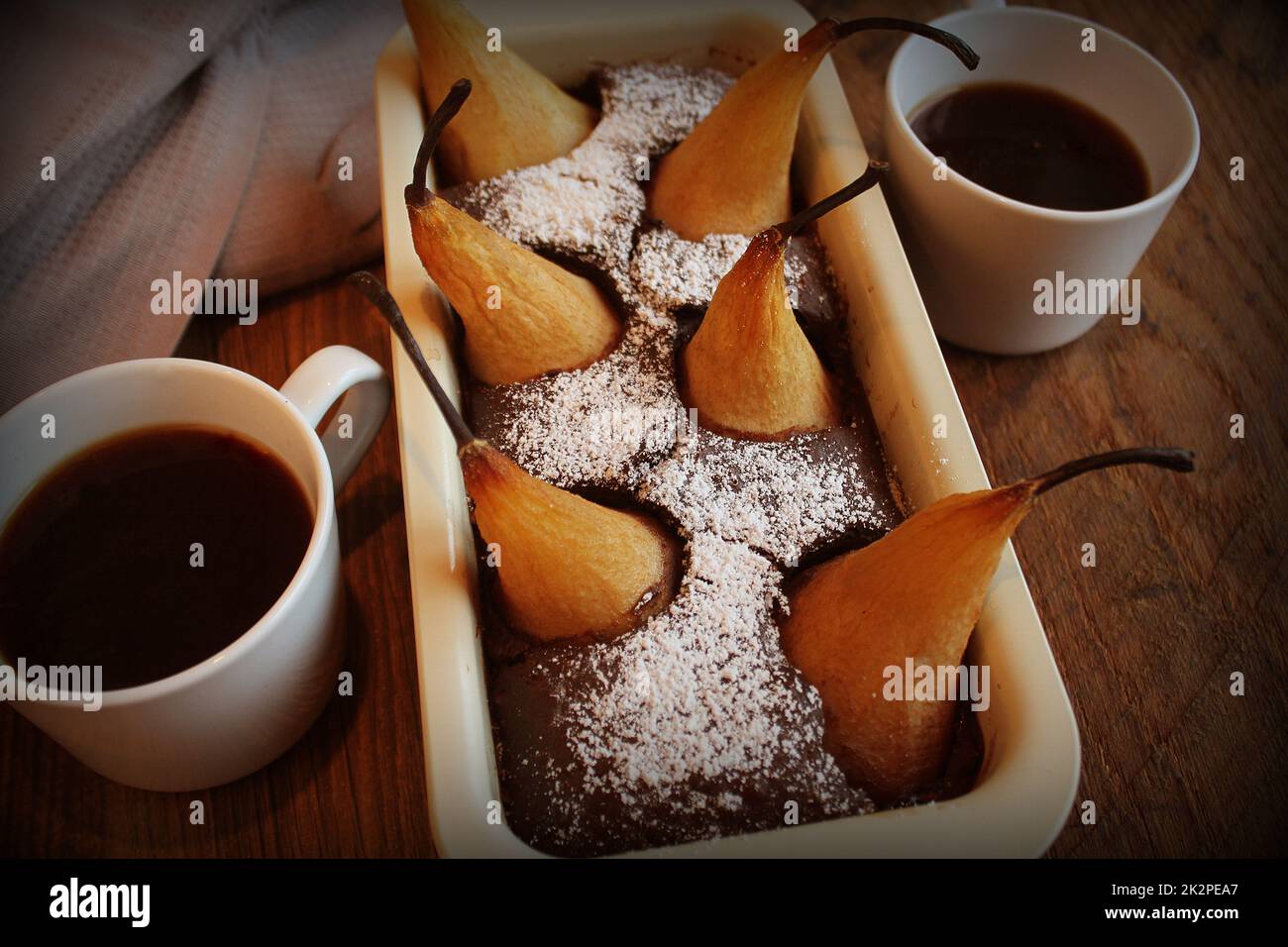 Gâteau de pain au chocolat avec des poires entières cuites à l'intérieur et deux tasses de café sur fond sombre. Vue d'en haut Banque D'Images