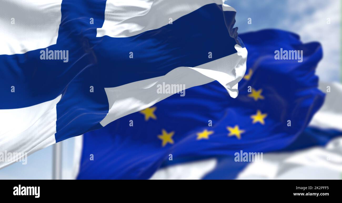 Détail du drapeau national de la Finlande qui agite dans le vent avec un drapeau flou de l'Union européenne en arrière-plan par temps clair Banque D'Images