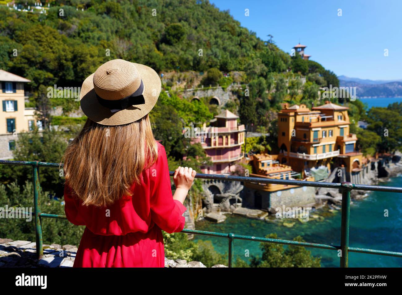 Voyage à Portofino. Vue arrière de la jolie fille dans l'élégante robe rouge et chapeau regardant les maisons sur les falaises suspendues à Portofino, Italie. Belle jeune femme en visite en Europe. Banque D'Images