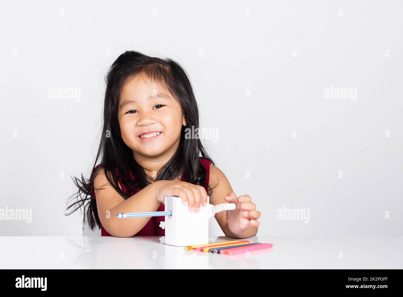 Petite petite petite fille mignonne 3-4 ans sourire à l'aide d'un taille-crayon tout en faisant des devoirs en studio photo isolée Banque D'Images