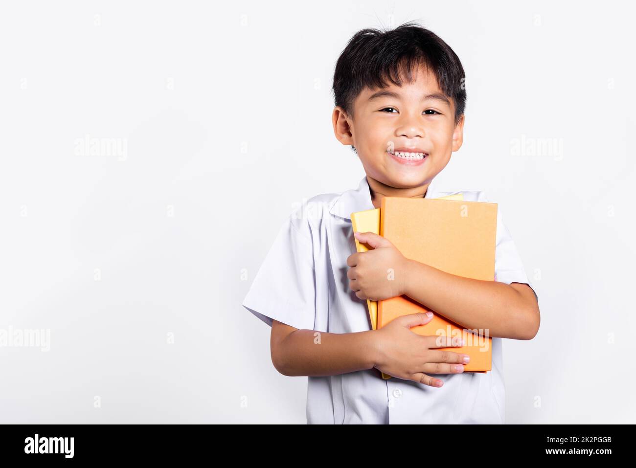 Asiatique adorable tout-petit souriant Happy Wear étudiant thaïlandais uniforme rouge pantalon tenir ou serrer livre Banque D'Images