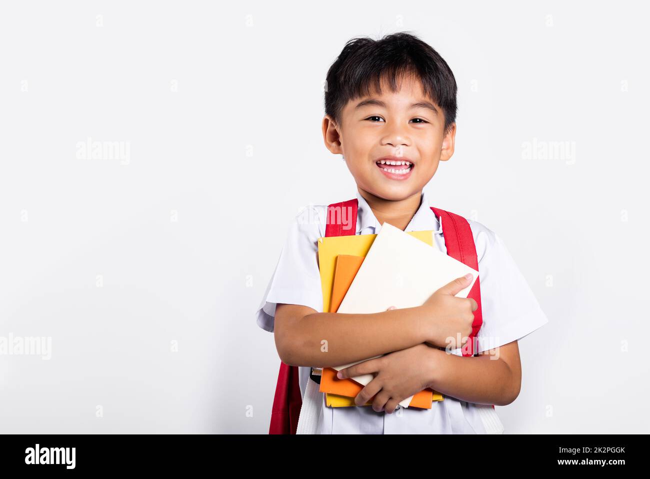 Asiatique adorable tout-petit souriant Happy Wear étudiant thaïlandais uniforme rouge pantalon tenir ou serrer livre Banque D'Images