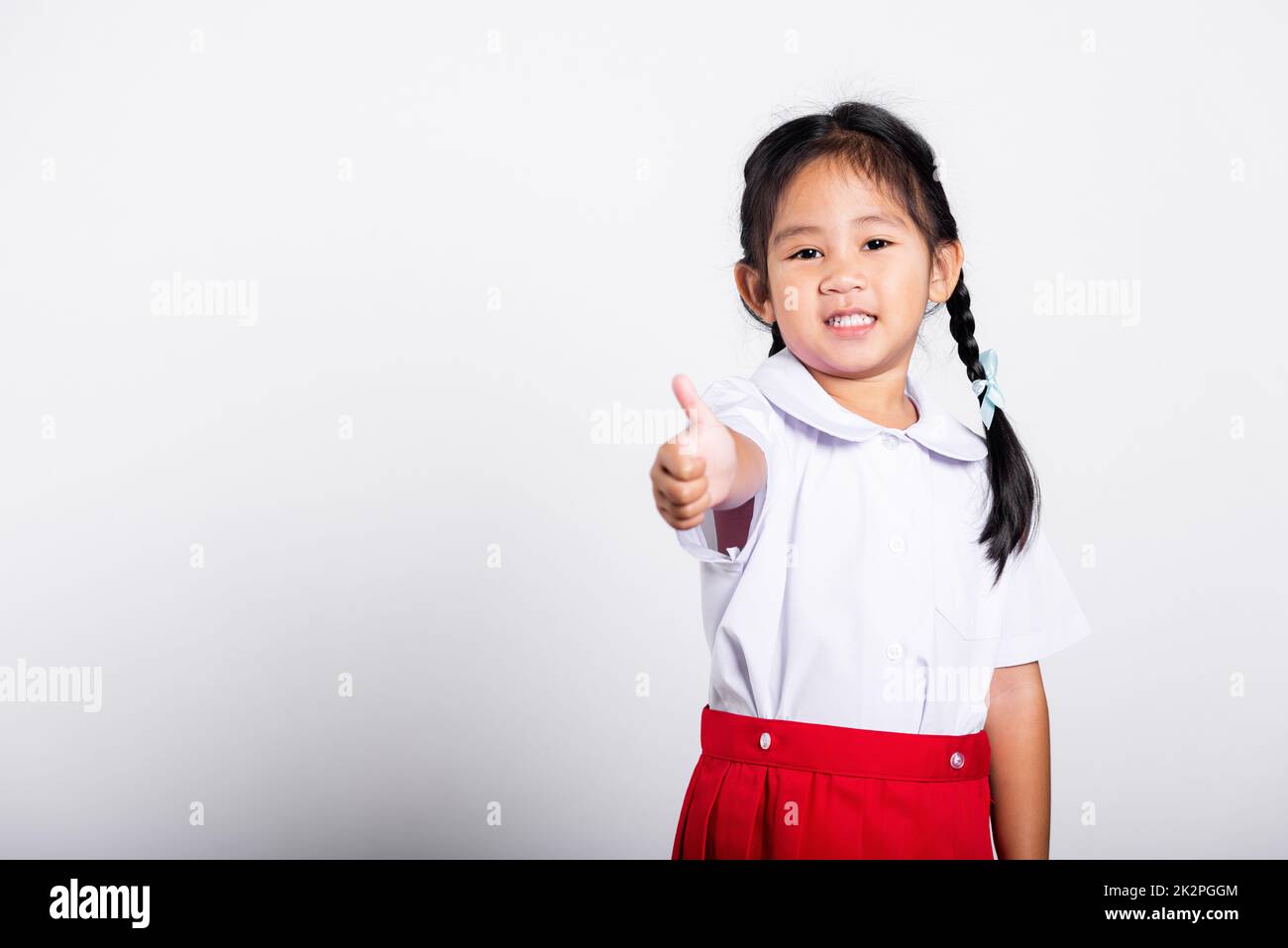 Asiatique adorable tout-petit souriant Happy Wear étudiant thaïlandais uniforme rouge jupe montrer pouce vers le haut de doigt Banque D'Images