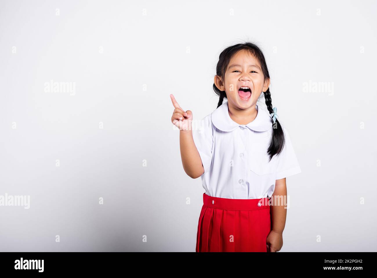 Asiatique tout-petit sourire Happy Wear étudiant thaïlandais uniforme rouge jupe continue de pointer le doigt sur l'espace de copie Banque D'Images