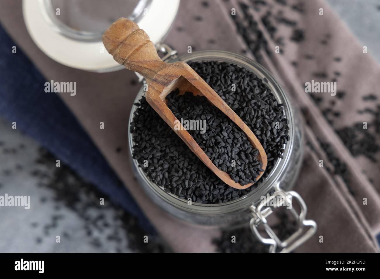 Épices indiennes graines de cumin noir (nigella sativa ou kalonji) dans un pot en verre avec vue sur le dessus de la pelle en bois Banque D'Images