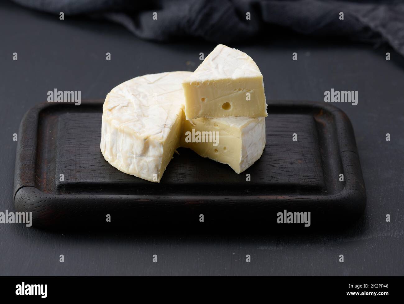 fromage brie rond sur planche à découper en bois brun, fond noir Banque D'Images
