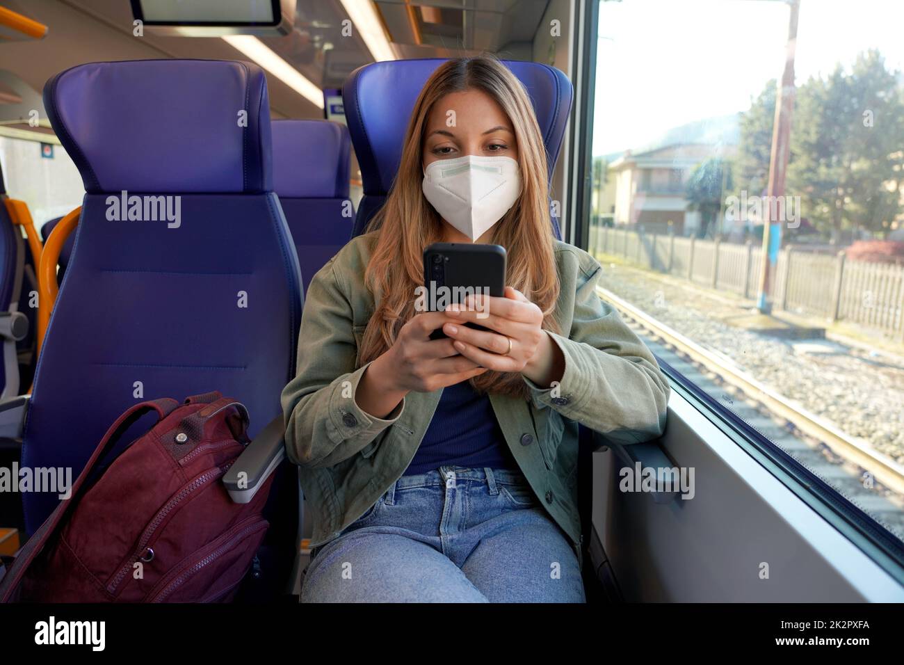 Une jeune fille étudiante portant un masque médical de protection sur le train en appréciant l'utilisation de l'application pour smartphone Banque D'Images