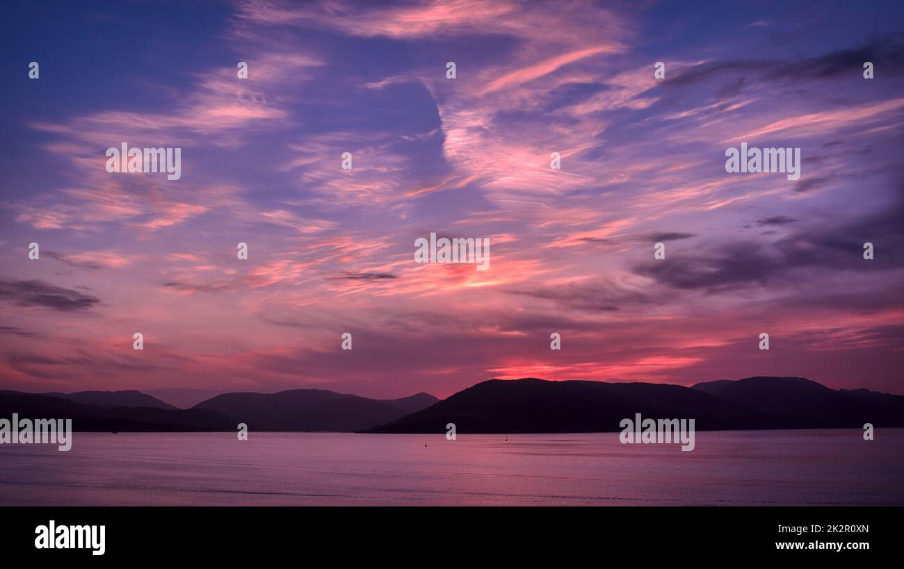 Coucher de soleil coloré, ciel rouge et bleu au-dessus d'une rivière et de collines. Banque D'Images