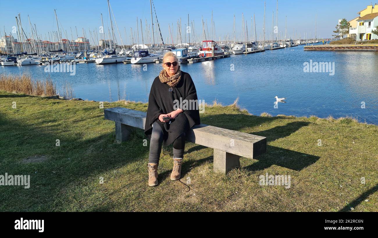 Portrait d'une femme blonde portant des lunettes de soleil assise sur un banc dans la marina Banque D'Images