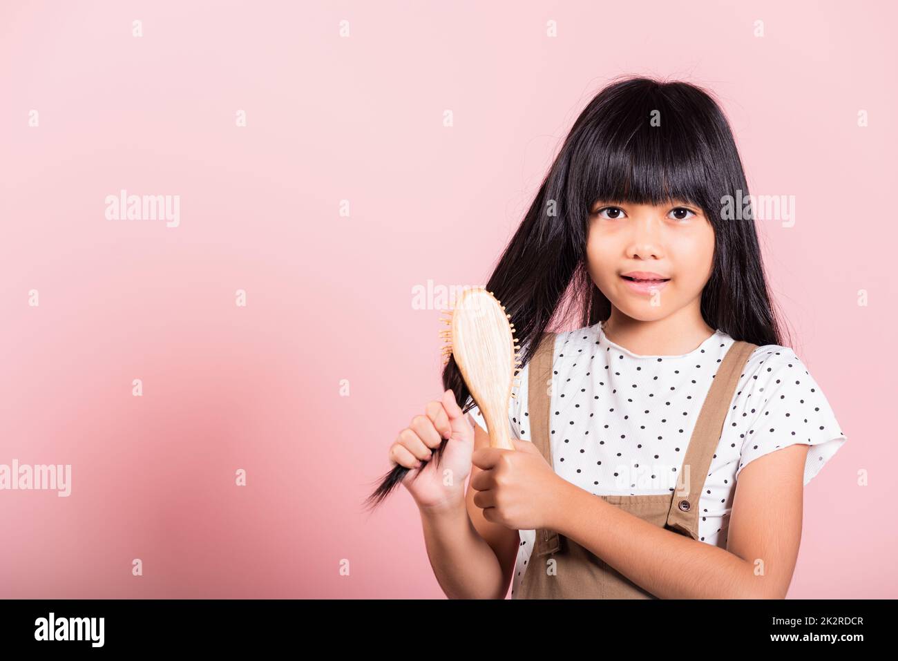 Petit enfant asiatique 10 ans tenir peigne se brossant de son indiscipliné elle touchant ses longs cheveux noirs Banque D'Images