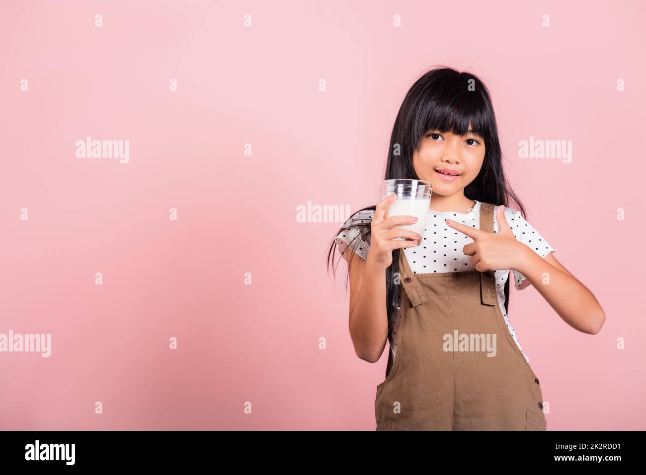 Petit enfant asiatique 10 ans sourire tenir le verre de lait boire du lait blanc et le doigt pointant Banque D'Images