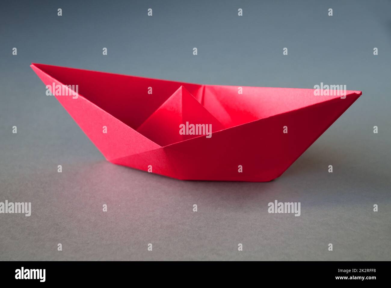 Bateau en papier rouge origami isolé sur un fond gris vierge. Banque D'Images