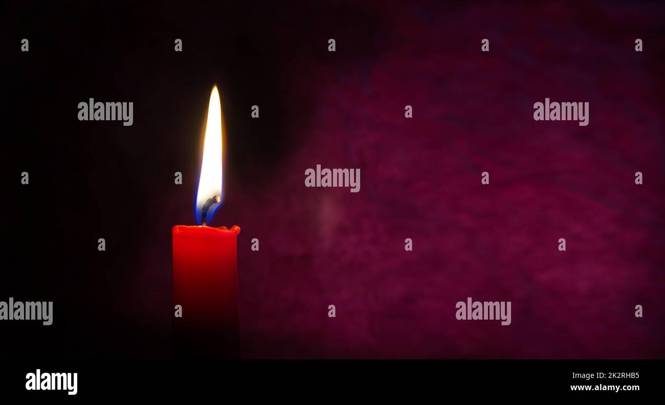 Bougie rouge allumée sur fond rouge foncé Banque D'Images