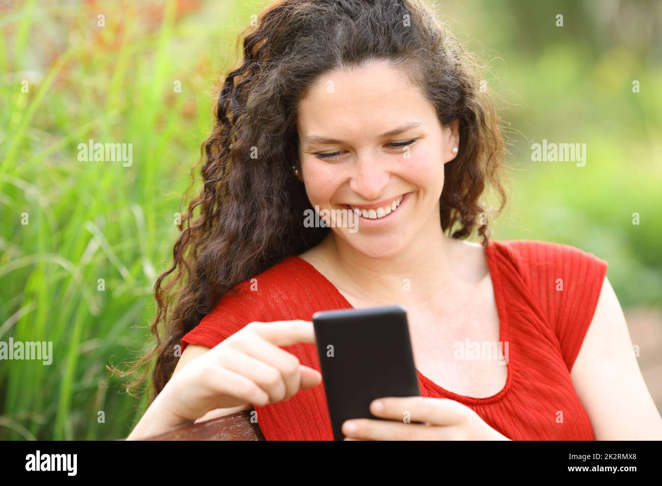 Une femme heureuse en rouge utilisant le téléphone dans un parc Banque D'Images