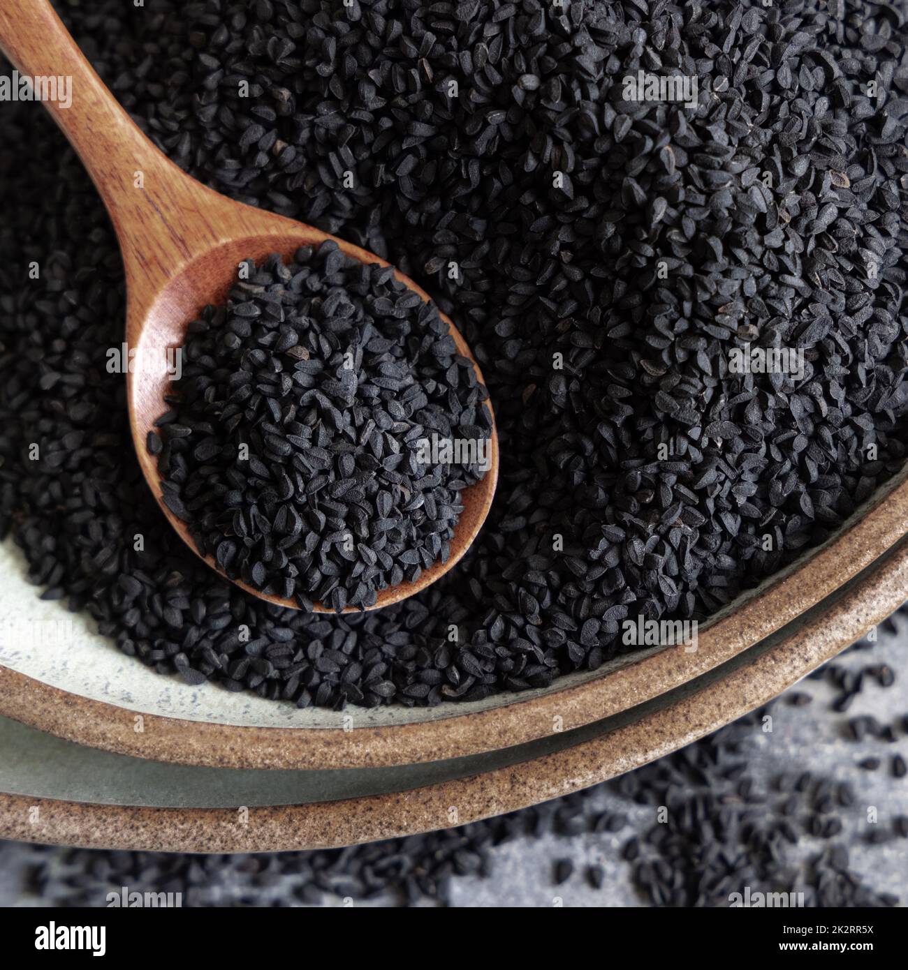 Assiette de graines de cumin noir d'épices indiennes (nigella sativa ou kalonji) à gros plan avec une cuillère en bois Banque D'Images