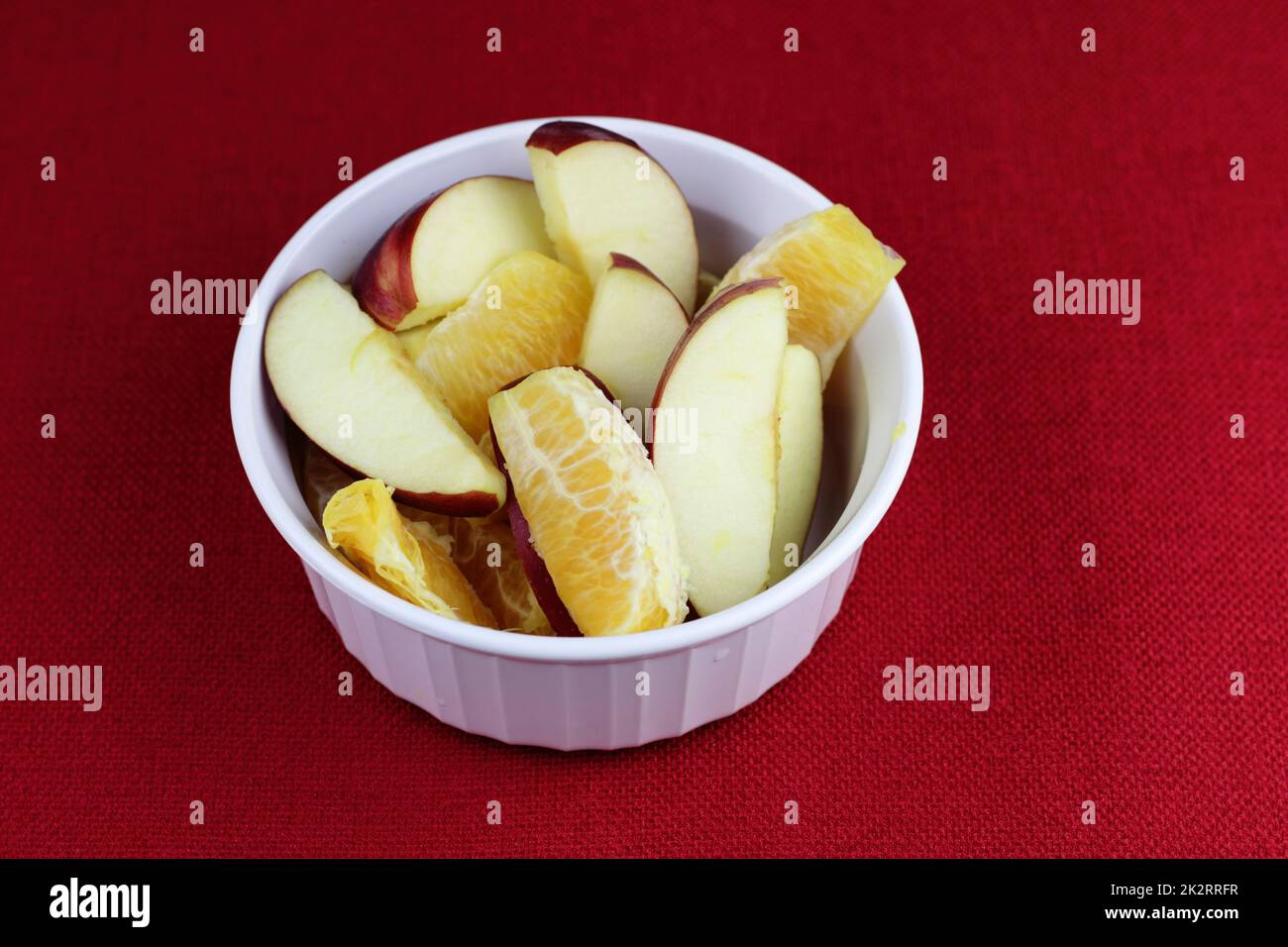 Sections de pomme rouge et de fruit orange dans un plat blanc sur fond rouge Banque D'Images