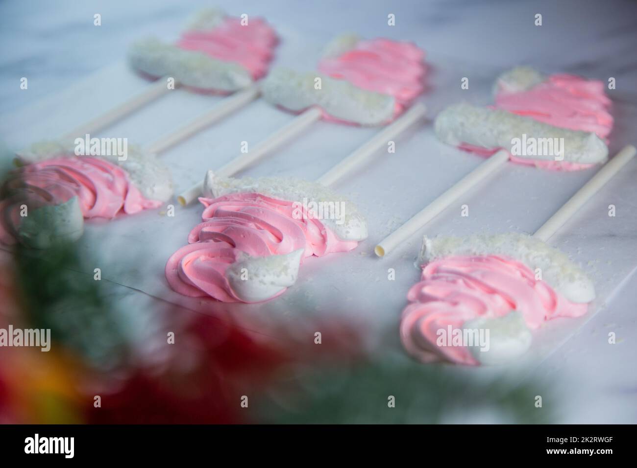 Meringue sous forme de chapeaux de Noël roses avec pompon et un revers blanc sur un bâton se trouvent sur parchemin blanc en deux rangées Banque D'Images