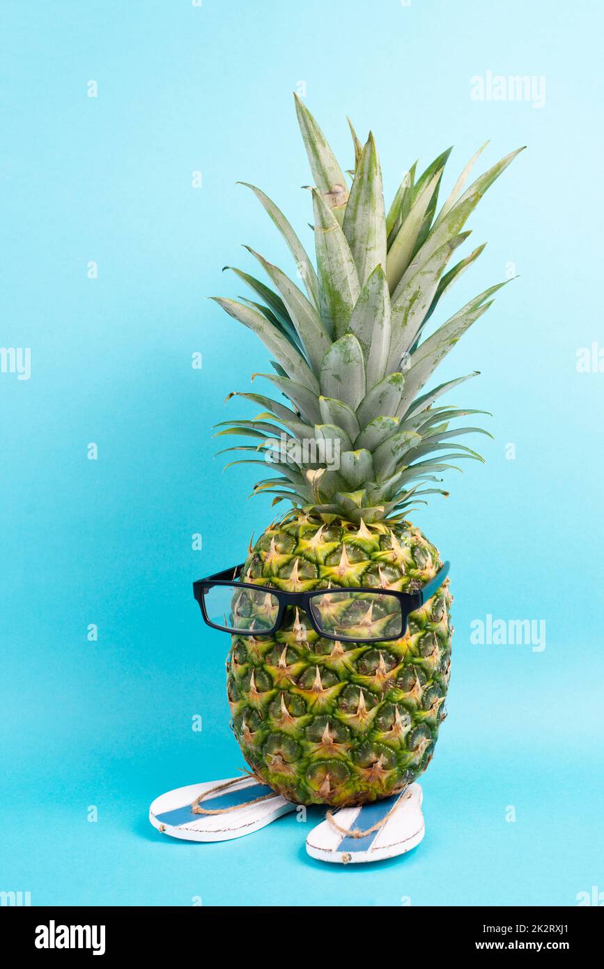 Ananas avec verres et tongs, concept de vacances et de voyage, vacances tropicales d'été, fruits drôles, fond bleu Banque D'Images