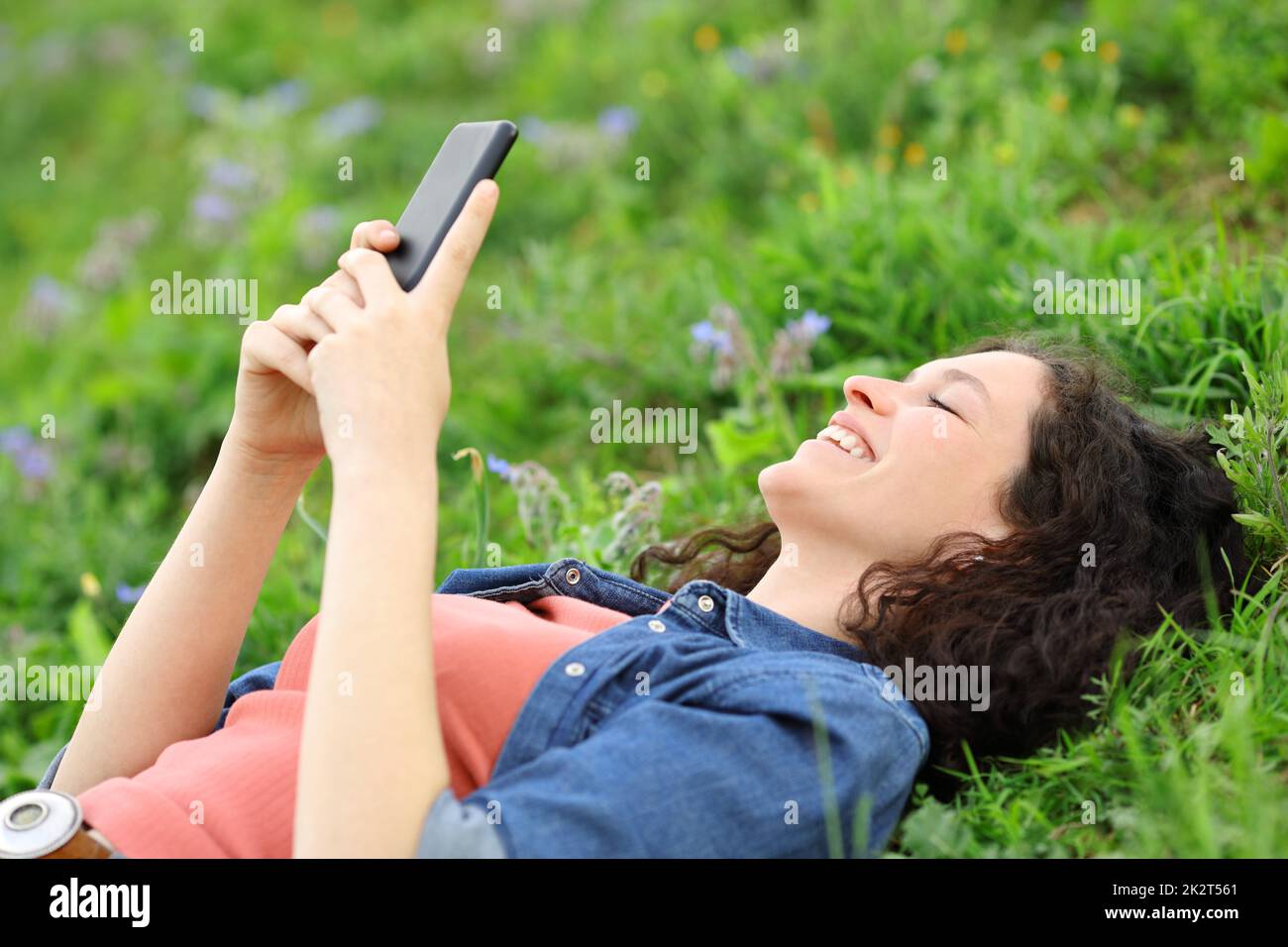 Bonne femme couchée sur l'herbe à l'aide du téléphone Banque D'Images