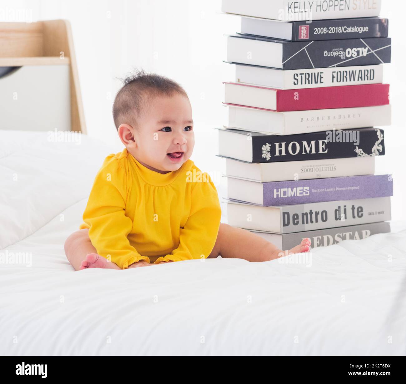 bébé petite fille tout-petit regardant une pile de livres sur le lit blanc de la chambre Banque D'Images